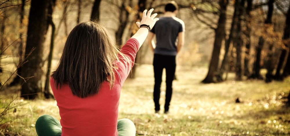 girl sitting on the ground reaching for her spouse who is walking away 