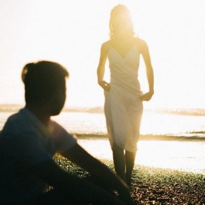 man sitting on sunset beach with woman approaching