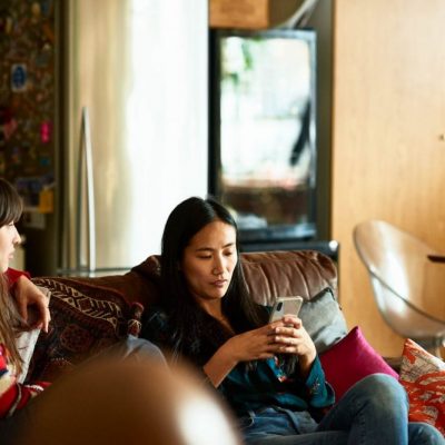 woman-sitting-on-sofa-with-friend-using-cell-phone